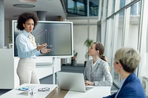 A leader presenting results to colleagues in a glass-walled office