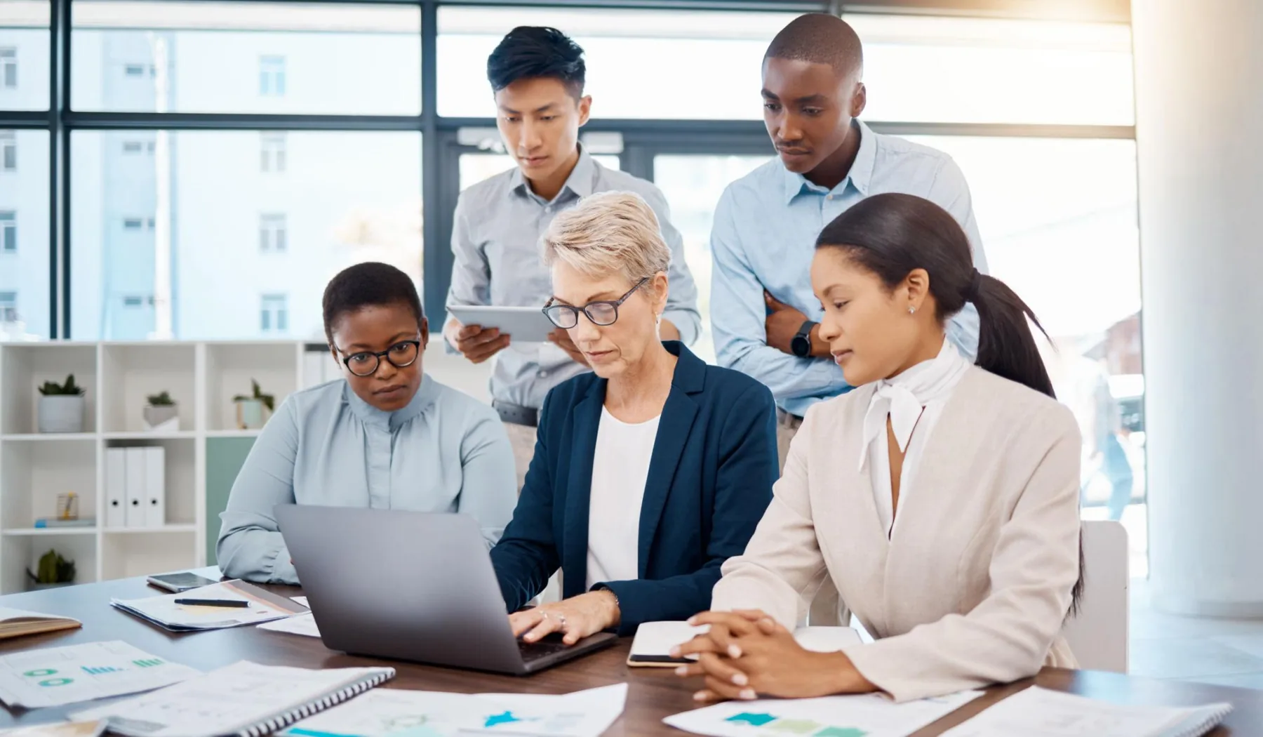 Colleagues working together at a laptop around a table of reports